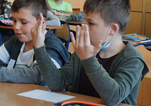 Na zdjęciu widać ucznia, który korzysta z umiejętności liczenia na palcach obu rąk podczas mnożenia liczb.