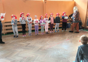 Uczniowe klas pierwszych dziewczynki i chłopcy pokazują pozostałym uczestniką znaki ostrzegawcze