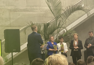 Zdjęcie grupowe przedstawiające liderów zwycięskich wniosków w ramach Budżetu Obywatelskiego 2022/2023 wraz z Prezydent Miasta Łodzi Hanną Zdanowską wręczającą dyplom z gratulacjami.