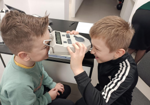 Uczniowie wykonują pomiar rozstawu źrenic za pomocą pupilometru.