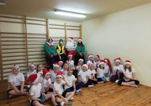 Grupa dzieci podczas zajęć wychowania fizycznego w towarzystwie Mikołaja i elfów