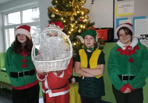 Uczniowie przebrani za Świętego Mikołaja i elfy przy choince szkolnej