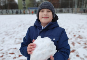 Chłopiec trzyma dużą kulę ulepioną ze śniegu