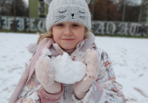Dziewczynka trzyma dużą kulę ulepioną ze śniegu