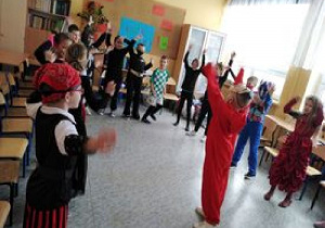 Zdjęcie przedstawia uczniów klasy IIa podczas balu karnawałowego. Uczniowie tańczą w kole i naśladują kroki taneczne demonstrowane przez jednego z nich.