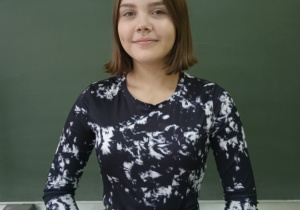 Na zdjęciu przewodnicząca Szkoły Podstawowej nr. 3 Oliwia Olszewka, na tle tablicy kredowej w sali lekcyjnej.