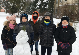 Zdjęcie przedstawia pięcioro uczniów z klas 3: czterech chłopców i jedną dziewczynkę. Dzieci stoją za ulepionym przez nie bałwanem, który składa się z trzech śnieżnych kul. W tle widać zabudowania i drzewa.